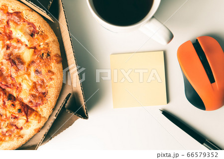 Pizza in box, cup of coffee, laptop, computer mouse, pen and empty sticker on table in office. Pizza in box, cup of coffee, laptop, computer mouse, pen and empty sticker on table in office. 66579352