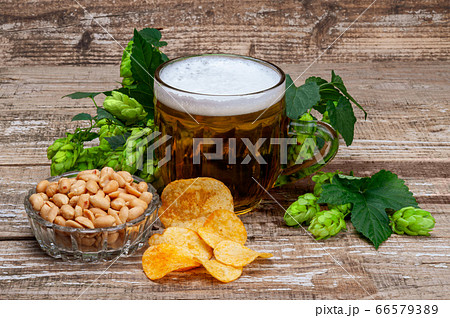 A glass of beer with green hops, peanuts and chips. 66579389