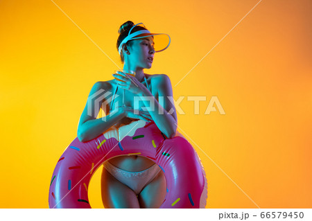 Fashion portrait of seductive girl in stylish swimwear posing on a bright yellow background. Summertime, beach season 66579450