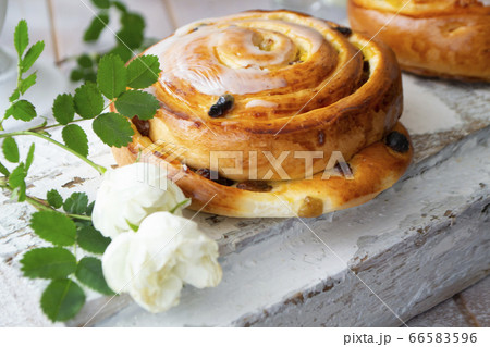 Raisin bun. Bun with raisins and vanilla cream close-up on white shabby background with vintage white roses Raisin bun. Bun with raisins and vanilla cream close-up on white shabby background with vintage white roses 66583596