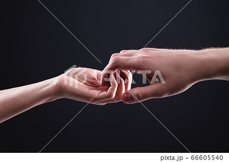 Two hands male and female ordinately hold each other symbolizing the help and mutual support between men and women on a black background studio shooting 66605540