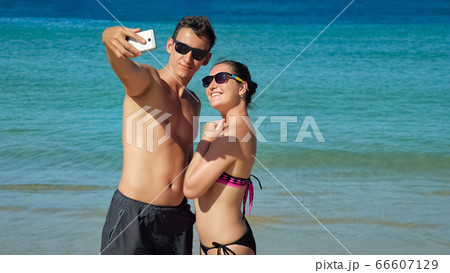 smiling happy couple makes selfie on sunny beach near azure ocean 66607129