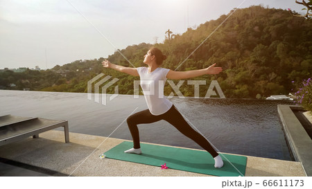 Yoga in the open air. Woman in a warrior pose near the pool Yoga in the open air. Woman in a warrior pose near the pool 66611173