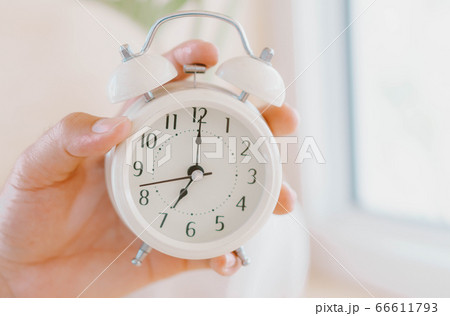 Closeup hand holding alarm clock on white table Closeup hand holding alarm clock on white table 66611793