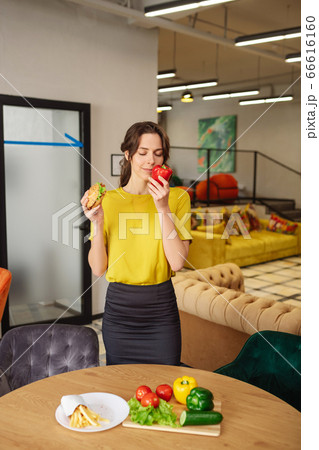 Woman with burger smelling red big pepper Woman with burger smelling red big pepper 66616160