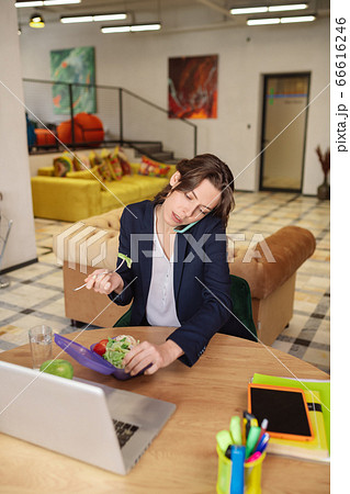 Girl talking on smartphone, behind laptop with fork and lunchbox. Girl talking on smartphone, behind laptop with fork and lunchbox. 66616246