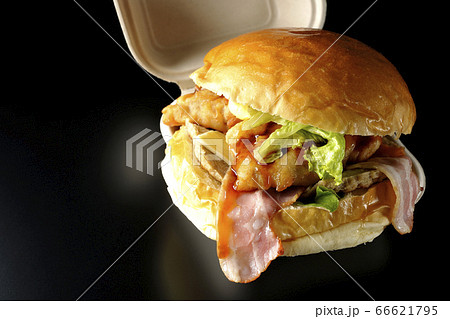 はみ出る美味さベーコンとレタスとチーズとチキンがサンドされた大きいハンバーガー（黒背景） 66621795