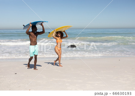 Mixed race couple holding surf boards on the beach 66630193