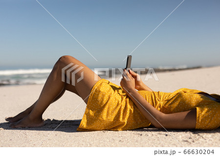 Mixed race woman using smartphone on the beach 66630204