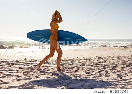 Young caucasian woman holding surf board on beach 66630245