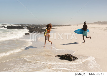 Mixed race couple holding surf boards on the beach Mixed race couple holding surf boards on the beach 66630247