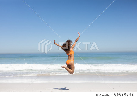 Mixed race woman jumping on the beach Mixed race woman jumping on the beach 66630248