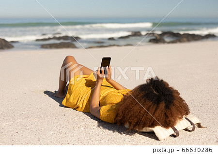 Mixed race woman using smartphone on the beach 66630286