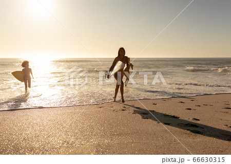 Young mixed race women holding surf boards on beach 66630315