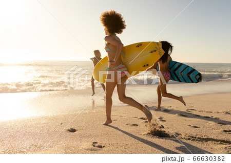 Young mixed race women holding surf boards on beach Young mixed race women holding surf boards on beach 66630382