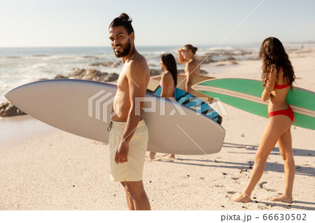 Mixed race people holding surf board on beach 66630502