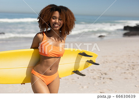 Mixed race woman holding a surfboard on the beach 66630639