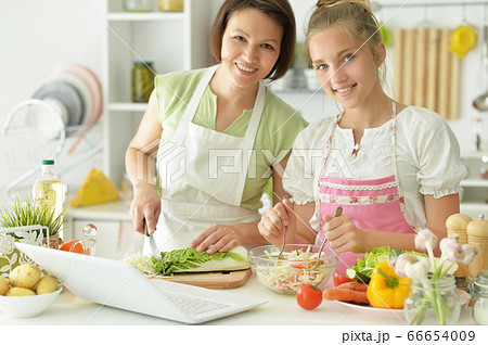 Cute little girl with mother cooking together at kitchen table 66654009