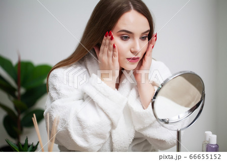 Skin care, young woman with pure face skin examines face in mirror Skin care, young woman with pure face skin examines face in mirror 66655152