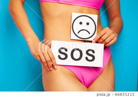 Woman health problem and menstruation pain, closeup of woman's hands holding a sad smile card near her belly 66655215