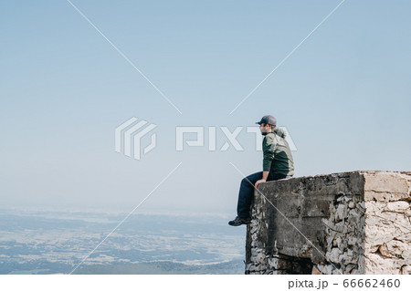 Man with cap sitting backside looking view from top of building. Man with cap sitting backside looking view from top of building. 66662460