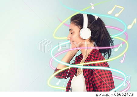 Energy girl with white headphones listening to music with closed eyes on blue background in studio. Energy girl with white headphones listening to music with closed eyes on blue background in studio. 66662472