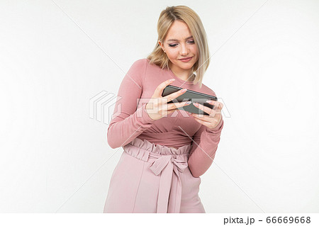 Caucasian blond girl in pink clothes plays on the phone in a horizontal position on a white 66669668