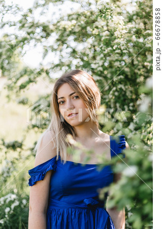 Sensual calm portrait of beautiful hipster woman in blooming bush with white flowers of spirea. Copy space. Stylish blonde woman in blue dress in garden 66678858