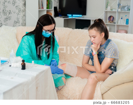A teenage girl with a knee injury at a trauma doctor's appointment, for bandaging abrasions. 66683205