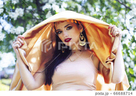young pretty indian girl in jewelry and veil posing cheerful happy smiling in green park, lifestyle people concept 66688714