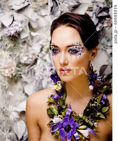 floral face art with anemone in jewelry, sensual young brunette woman in studio close up 66688939