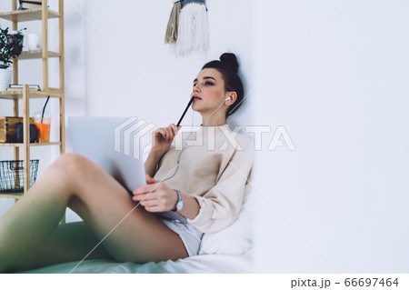 Pensive woman sitting on bed with computer Pensive woman sitting on bed with computer 66697464