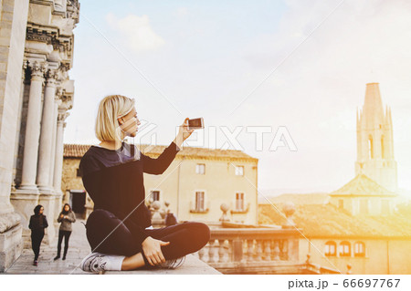 Young beautiful woman with good mood is talking on mobile phone, while is sitting on a building roof. 66697767