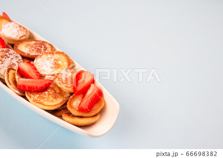 Close up of mini pancakes cereal with strawberries on white plate on blue background with copy space for recipe or your text. Breakfast concept, trendy food Close up of mini pancakes cereal with strawberries on white plate on blue background with copy space for recipe or your text. Breakfast concept, trendy food 66698382