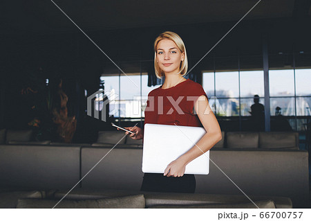 Smiling young businesswoman looking at camera while holding on her knees open laptop computer 66700757