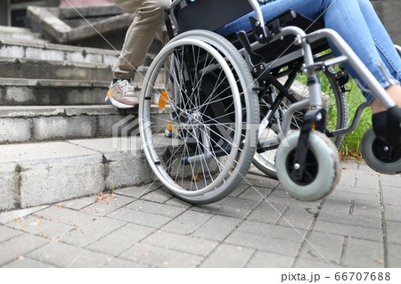 Social worker helps disabled person in wheelchair climb stairs 66707688