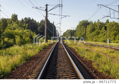 An empty railway stretching into the distance in the warm sunlight. Walking through the green forest. Travel tourism summer vacation hiking trekking adventure. 66711773