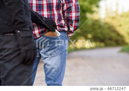 The thief in black clothes and gloves stealing a wallet with money from pocket. Pickpocketing on the street during daytime. 66712247
