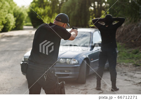 The policeman is targeting an offender near the stolen car. Stop criminality. The policeman is targeting an offender near the stolen car. Stop criminality. 66712271