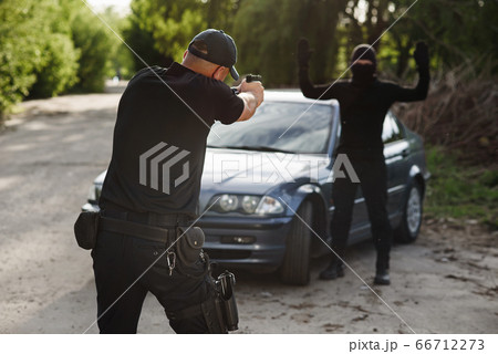 The policeman is targeting an offender near the stolen car. Stop criminality. The policeman is targeting an offender near the stolen car. Stop criminality. 66712273