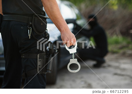 The police officer holding handcuffs in his hands. The policeman arrested the offender who stole the car. The police officer holding handcuffs in his hands. The policeman arrested the offender who stole the car. 66712295