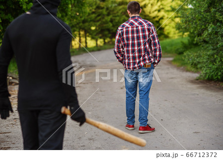 An offender in black clothes with a baseball bat in his hands attacks a man. Pickpocketing on the street during daytime. 66712372