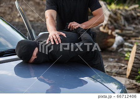 A police officer arrested the offender in a mask with a stolen car and handcuffed him on the hood of the car. 66712406
