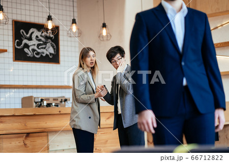 Two coworkers Staring and Gossiping About Their Male Colleague Two coworkers Staring and Gossiping About Their Male Colleague 66712822