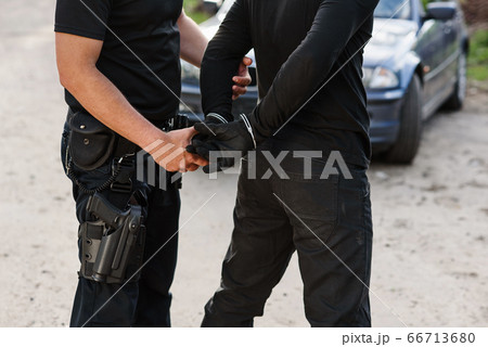 A police officer arrested an offender with the stolen car and handcuffed him close up. 66713680