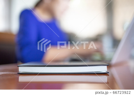 Selected focus on notebook on the table with woman woking on laptop in blur background. Selected focus on notebook on the table with woman woking on laptop in blur background. 66723922