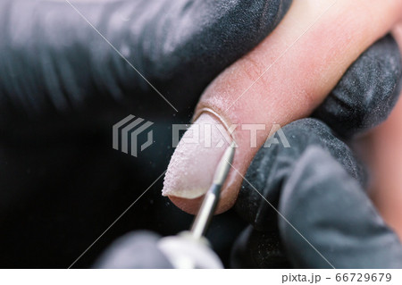 Close-up shot of hardware manicure in a beauty salon. Manicurist is applying electric nail file drill to manicure on female fingers. Close-up shot of hardware manicure in a beauty salon. Manicurist is applying electric nail file drill to manicure on female fingers. 66729679