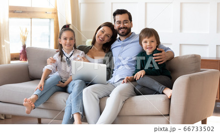 Portrait smiling parents with children sitting on couch with laptop Portrait smiling parents with children sitting on couch with laptop 66733502