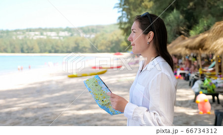 lady in white shirt stands on beach and looks at map follows pointers 66734312