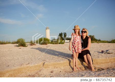 Smiling mother and beautiful daughter having fun on the beach. Portrait of happy woman giving a piggyback ride to cute little girl with copy space. Portrait of kid embracing her mom during summer. 66735742
